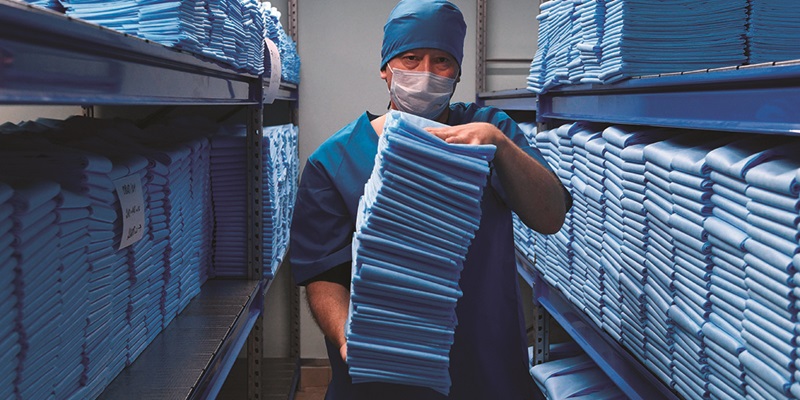 Person in medical uniform and mask holding a pile of medical uniforms