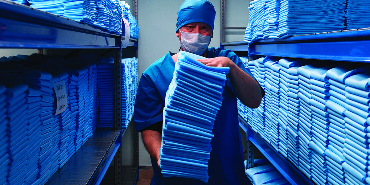 Person in medical uniform and mask holding a pile of medical uniforms